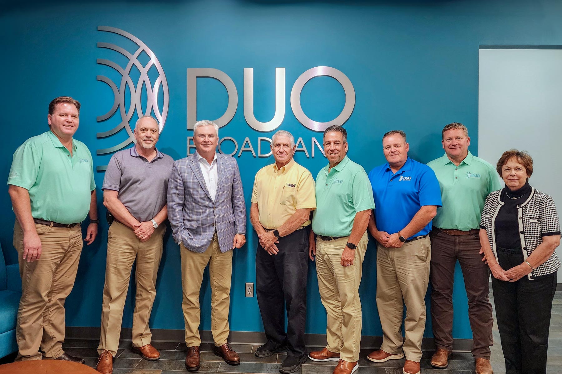 Group of 8 people in front of a wall with DUO Broadband logo